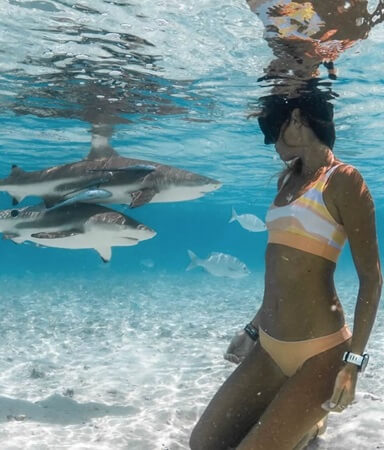 woman in light orange bikini swimming with two sharks underwater
